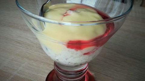Ein Dessertbecher enthält Hafer-Reis-Dessert mit einer Schicht Vanilletopping und einem fruchtigen Sirup.