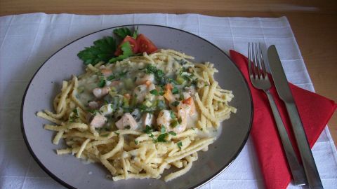 Ein Teller mit Lachs-Scampi-Ragout liegt auf einem Tisch, umgeben von einer Gabel, einem Messer und einer roten Serviette.