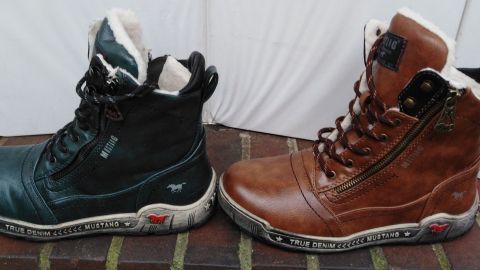 Schwarze und braune Stiefel stehen nebeneinander auf einem Boden, bereit zum Reinigen von Imprägnierspray-Flecken.