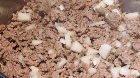Hackfleisch verdirbt selbst im Kühlschrank sehr schnell - man sollte es gleich verbrauchen! Verbrauchen heißt aber garen oder braten, und nicht gleich alles auffuttern, dann kann man es einfrieren. Braun gebratenes Hackfleisch mit Zwiebelstücken wird in einer Pfanne zubereitet und zeigt eine leckere Kochsituation.