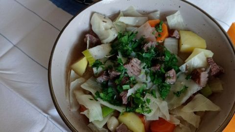 Ein buntes Gericht aus Dithmarscher Weißkohl mit Fleisch und Gemüse in einer Schüssel, daneben frische Brötchen in einem Korb.