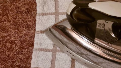 Ein Dampfbügeleisen wird auf einem Handtuch platziert, um Druckstellen von Möbeln im Teppich zu entfernen.