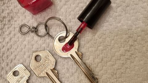 Ein roter Nagellack wird auf den Schlüssel auf einem weichen, hellen Untergrund aufgetragen, um Schlüssel zu kennzeichnen.