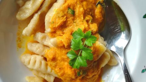 Spätzle liegen auf einem Teller, überzogen mit orangefarbener Sauce und garniert mit frischem Koriander.