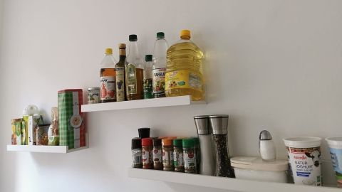 Auf einer weißen Wand sind verschiedene Flaschen und Gewürze auf einer Bilderleiste angeordnet, die Ordnung ins Küchenregal bringen.