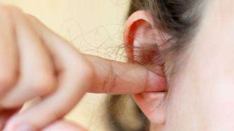 Ein Finger steckt in einem Ohr, während die Person zur Linderung von Schluckauf eine Technik anwendet.
