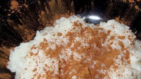 Wei&szlig;er Milchreis steht in einer schwarzen Sch&uuml;ssel, garniert mit Zimt, in einer gem&uuml;tlichen K&uuml;chenumgebung.