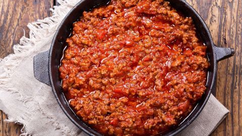 Eine Pfanne zeigt eine reichhaltige, rote Bolognese nach Mamma Rosa, die auf einem rustikalen Holztisch serviert wird.