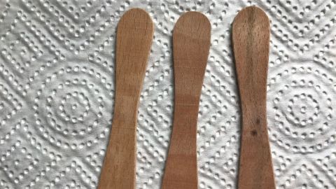Drei Holz-Eisstiele liegen ordentlich auf einem weißen Papiertuch, bereit für hygienisches Entnehmen von Creme.