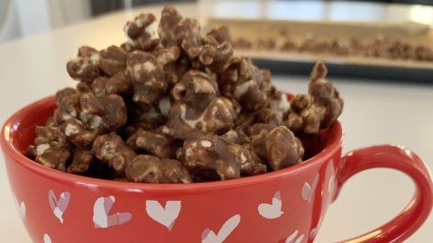 Eine rote Herz-Tasse ist gefüllt mit Nutella-Popcorn, das köstlich aussieht, auf einem weißen Tisch mit etwas Popcorn daneben.