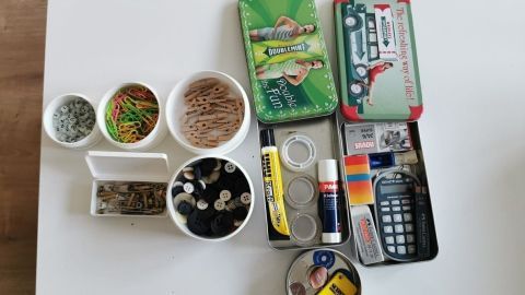 Auf einem Tisch sind verschiedene Behälter mit Kleinigkeiten wie Knöpfen, Büroklammern und Kleber ordentlich angeordnet.