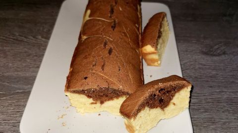 Ein Marmorkuchen liegt auf einem weißen Teller, während ein Stück davon abgeschnitten und daneben platziert ist.