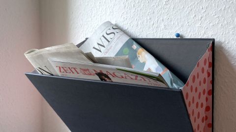 Ein Zeitschriftenhalter aus einem alten Bucheinband hängt an der Wand und hält mehrere Zeitschriften und Zeitungen.