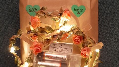 Ein liebevoll verpacktes Geschenk aus braunem Papier mit Lichtern, Blumen und herzförmigen Aufklebern.