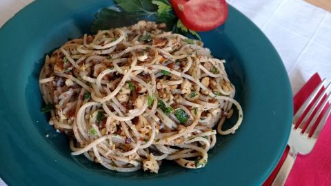 Ein Teller mit Spaghetti, garniert mit Walnüssen und Tomate, liegt auf einem Tisch mit roter Serviette und Besteck.