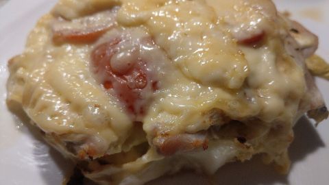 Ein überbackenes Huhn liegt auf einem Bett aus Kohl, bedeckt mit geschmolzenem Käse und speckigen Tomatenscheiben.
