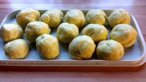 Auf einem weißen Teller liegen gleichmäßige, gelbe Kartoffelknödel, frisch zubereitet, auf einem Holzuntergrund.