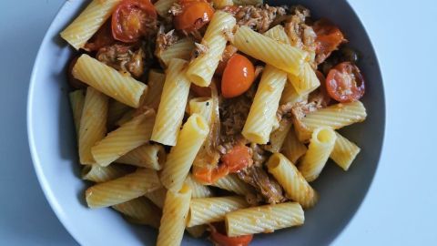 Ein Teller Rigatoni al Tonno mit Tomaten, angerichtet auf einem weißen Tisch, zeigt eine leckere Pasta-Mahlzeit.