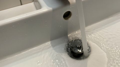 Ein glänzender Wasserhahn lässt Wasser in ein Waschbecken laufen, während die fließende Strömung auf der Wasseroberfläche spritzt.
