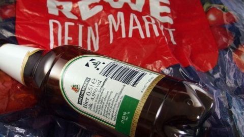 Pfandflaschen vorsortieren: Je eine Tüte von Aldi, Lidl, Penny, Plus usw. besorgen und die leeren Flaschen gleich in die jeweils passende Tüte einsortieren. Eine Pfandflasche liegt auf einer roten REWE-Tüte, umgeben von einem bunten Hintergrund.