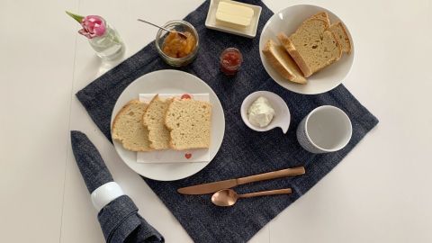 Auf einem blauen Tuch liegen frische Zwiebackscheiben, Marmelade, Butter und ein Kaffeebecher, ideal zum Frühstück.