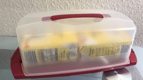 Eine Kuchenbox steht auf einem Tisch und enthält Zutaten wie Weizenmehl. Sie ist transparent und hat einen roten Deckel.