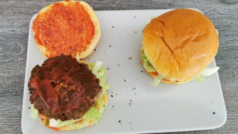 Zwei unvollständige Burgerbuns liegen auf einem Teller, einer mit Hackfleisch und Gemüse belegt, der andere frisch.