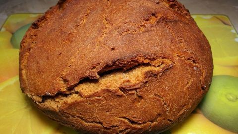 Ein frisch gebackenes Brot liegt auf einer bunten Unterlage, die mit Früchten verziert ist. Es hat eine goldene, knusprige Kruste.
