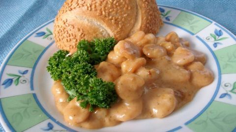 Sahne-soße über zarten Shrimps, umgeben von frischer Petersilie und einem Sesambrötchen auf einem dekorativen Teller.