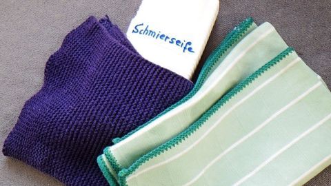Ein Reinigungstuch und eine Flasche mit Schmierseife liegen zusammen auf einer grauen Oberfläche, bereit zum umweltfreundlichen Reinigen.
