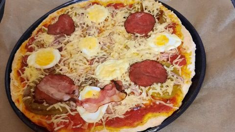 Eine Pizza mit Ei liegt auf einem Backblech, goldbraun gebacken, belegt mit Käse, Speck und mehreren Eiern.
