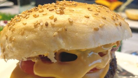 Ein Burgerbrötchen mit Sesam, gefüllt mit einem saftigen Patty, Käse und frischem Gemüse, auf einem weißen Teller.