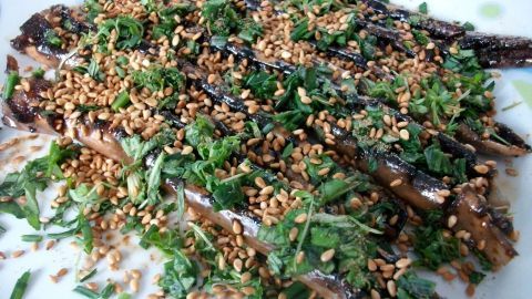 Gebackene Teriyaki-Auberginen liegen auf einem Teller, garniert mit Sesam und frischem Grün in einem hellen Raum.
