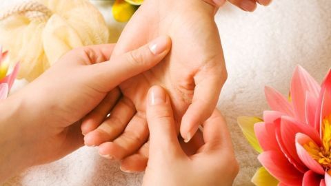 Eine Handmassage wird zwischen zwei Händen durchgeführt, um Entspannung zu fördern, umgeben von Blumen.
