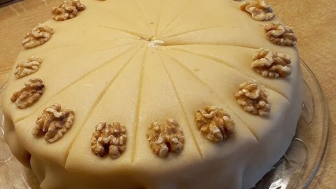 Eine runde Marzipan-Nuss-Torte liegt auf einem durchsichtigen Teller und ist mit Walnüssen dekoriert, ideal für Ostern.