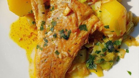Kabeljau liegt auf einem Bett aus Spitzkohl und Kartoffeln, umgeben von goldener Curry-Butter, appetitlich angerichtet.
