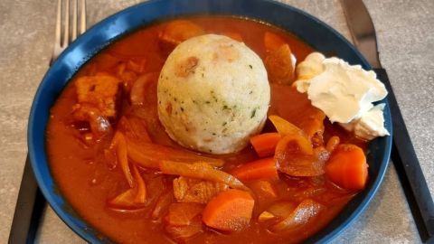 Saftiges Tomatengulasch mit zartem Fleisch und einem großen Knödel auf einem blauen Teller in einer gemütlichen Küche.