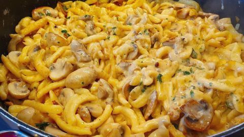 Goldene Spätzle mit Champignons schwimmen in einer cremigen Rahmsauce in einer tiefen Pfanne, garniert mit Kräutern.