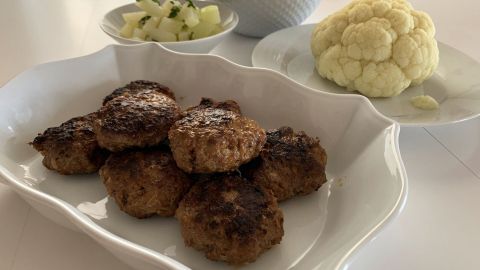Saftige Frikadellen sind auf einem rustikalen Teller angerichtet, umgeben von Blumenkohl und Salatbeilagen.