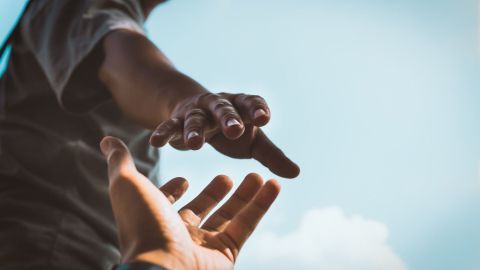 Eine Hand streckt sich aus, um eine andere zu erreichen, vor einem klaren Himmel, der Unterstützung symbolisiert.
