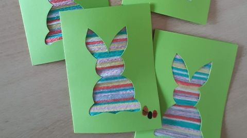 Bunte Osterkarten aus grünem Papier zeigen Hasen mit Wolle, die auf einem hellen Tisch angeordnet sind.