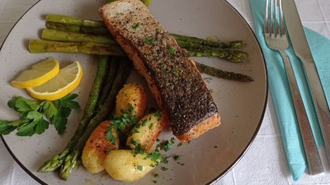 Ein köstlicher Lachs liegt auf einem Teller, umgeben von gebratenem Spargel, Kartoffeln und Zitronenscheiben.