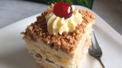 Eine üppige Frankfurter Kranz Schnitte liegt auf einem weißen Teller, dekoriert mit Sahne und einer Kirsche, umgeben von österlicher Deko.