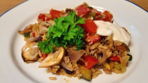 Eine Gemüse-Reispfanne mit Basmati-Reis wird auf einem weißen Teller serviert, umgeben von frischen Zutaten und einer Holzplatte.