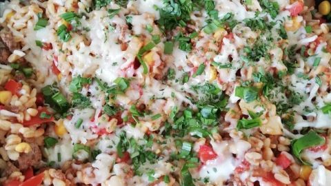 Eine bunte Gemüsepfanne mit Hackfleisch und Ebly, bedeckt mit Käse und frischen Kräutern, in einer Pfanne angerichtet.