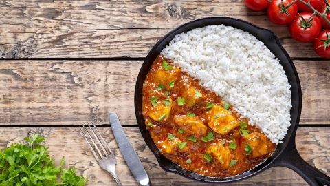 Ein Pfannen-Gericht zeigt Reisfleisch mit Pilzen und Paprika, angerichtet mit frischem, grünen Koriander auf Holzuntergrund.