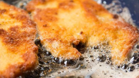 Zwei goldbraune Wiener Schnitzel braten in einer Pfanne, umgeben von sprudelndem, heißem Öl und knuspriger Textur.