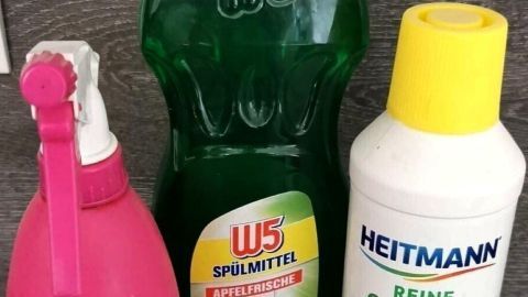 Grüner Allzweckreiniger und Zitronensäure stehen neben einer Sprühflasche in einer modernen Küchenumgebung.