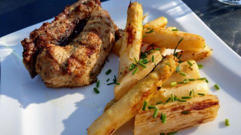 Gegrillter Spargel liegt appetitlich auf einem weißen Teller neben zartem Fleisch, umgeben von frischem Schnittlauch.