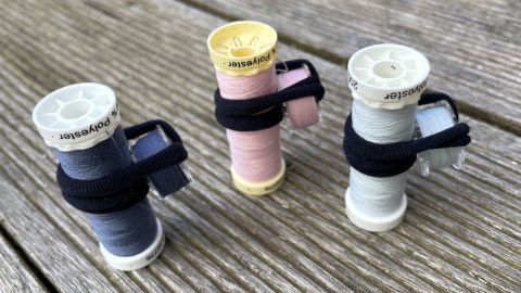 Drei Unterfadenspulen sind mit einem Band zusammengebunden und stehen auf einer Holzoberfläche.